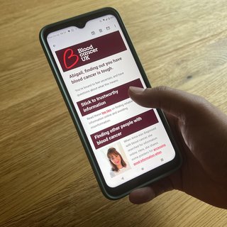 Photo of a hand holding a smart phone, looking at an email that talks about blood cancer information and support.