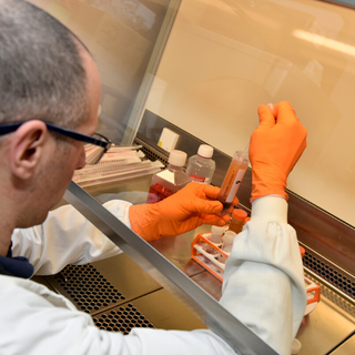 A researcher in a laboratory holding a vial filled with blood and a pipette