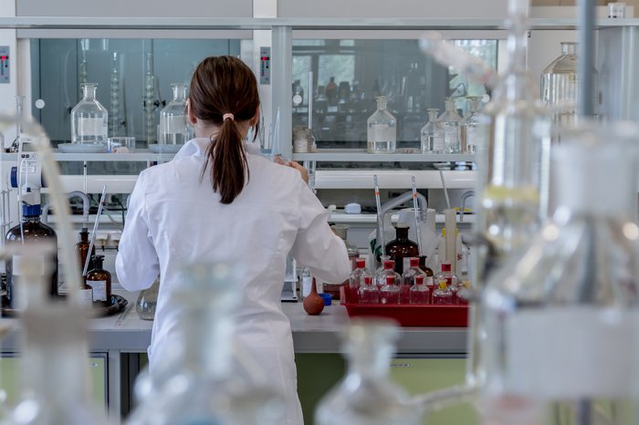 A researcher stands in a laboratory at a work bench surrounded by sample jars