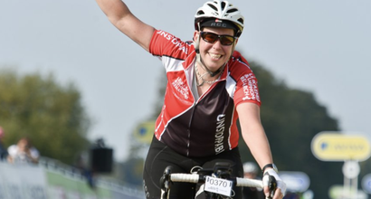 Sarah, who was diagnosed with chronic lymphocytic leukaemia (CLL), raising one arm whilst cycling and smiling at the camera.