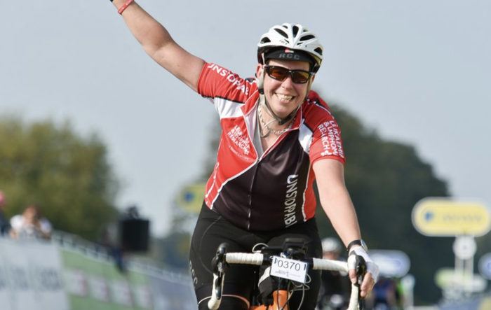 Sarah, who was diagnosed with chronic lymphocytic leukaemia (CLL), raising one arm whilst cycling and smiling at the camera.