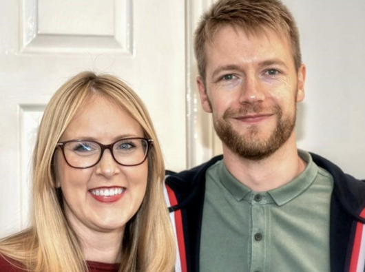 Emma, who was diagnosed with acute lymphoblastic leukaemia (ALL), smiling next to her partner in front of a wooden door.