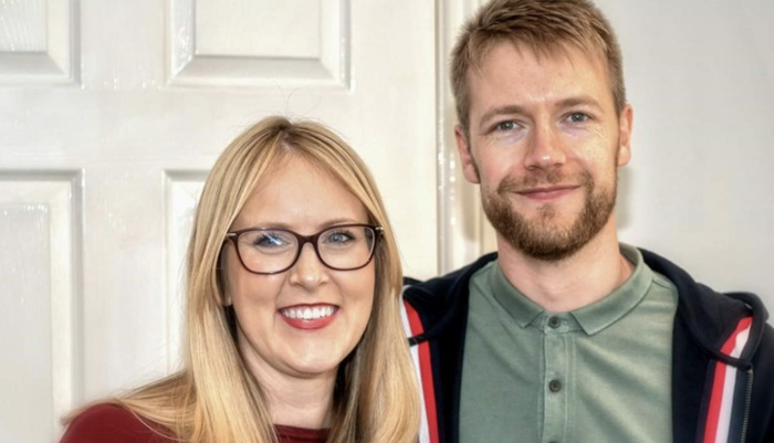 Emma, who was diagnosed with acute lymphoblastic leukaemia (ALL), smiling next to her partner in front of a wooden door.