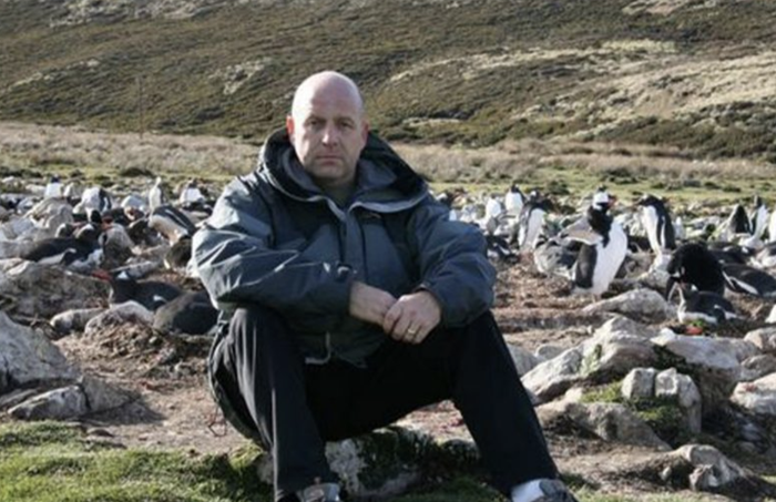 Edward, a retired soldier who was diagnosed with myeloma, sitting on a rock on a hiking trail looking straight faced at the camera.