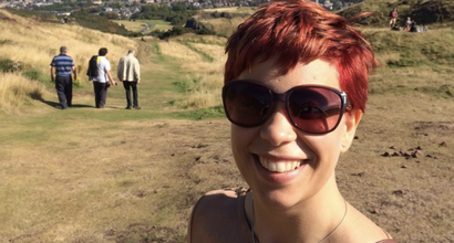 Emma, who was diagnosed with a myelodysplastic syndrome (MDS), smiling with sunglasses on up a hill with a city view in the background.