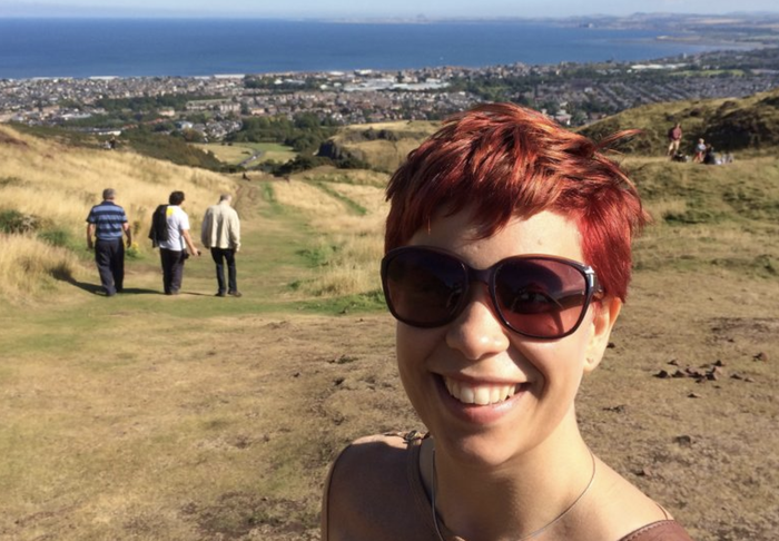 Emma, who was diagnosed with a myelodysplastic syndrome (MDS), smiling with sunglasses on up a hill with a city view in the background.