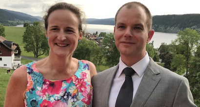 Carina, who was diagnosed with hairy cell leukaemia, standing on grass wearing formal clothes next to a man with sea and hills in the background.