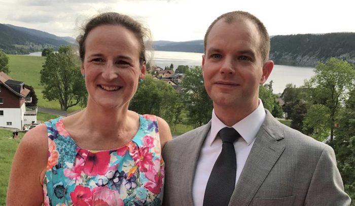 Carina, who was diagnosed with hairy cell leukaemia, standing on grass wearing formal clothes next to a man with sea and hills in the background.