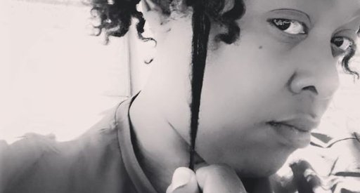 Black and white photograph of Simone, with medium length curly hair, looking serious and pulling at one curl.