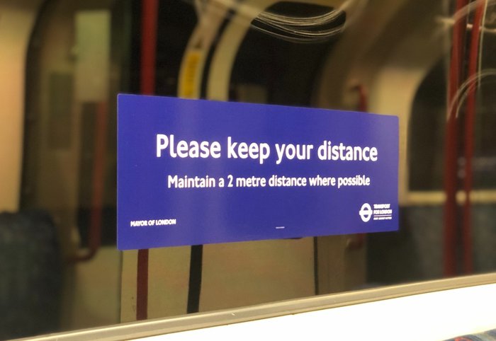 Transport for London sticker on the window of an underground train displaying text to keep a 2 metre distance from others.