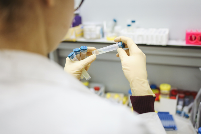 Back shot of a researcher in a lab looking closely at test tubes in their hand.