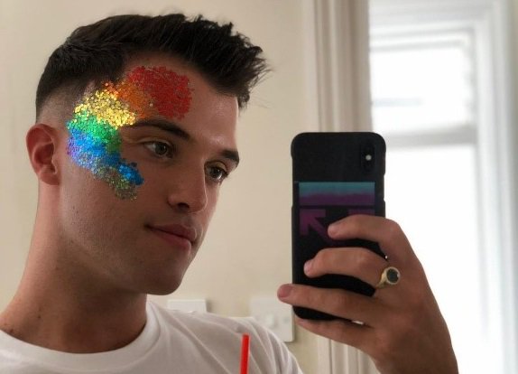 Todd Cooper, a Blood Cancer UK supporter, taking a photo in a mirror with rainbow glitter on forehead and cheek.