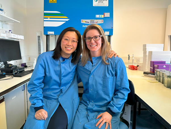 Two women in blue lab coats sitting and smiling