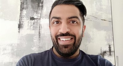 Vij, who was diagnosed with polycythaemia vera (PV), smiling into the camera in front of a large canvas painting on the wall.