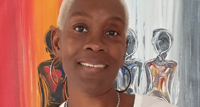 Yvonne, who was diagnosed with acute myeloid leukaemia (AML), smiling at the camera in front of a large, colourful painting of figures.