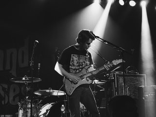 A black and white image of a guitarist on stage playing an electric guitar.