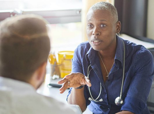 Doctor with a stethoscope around their neck talks to patient about their blood cancer.