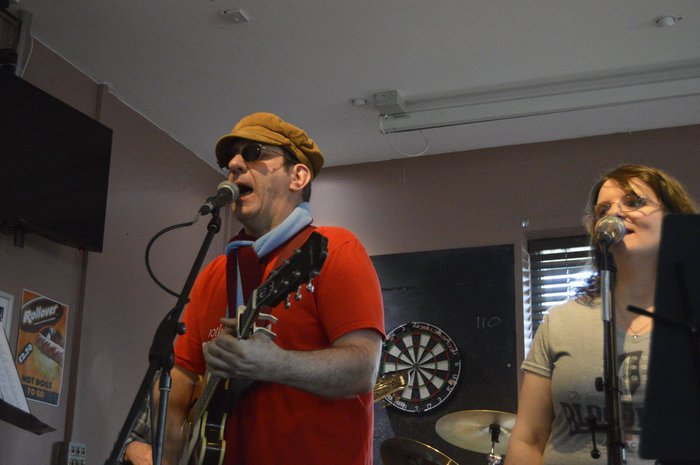 Ed Jones, who was diagnosed with leukaemia in 2006, is playing a guitar at a charity concert in Milton Keynes. He is standing at a microphone and singing.