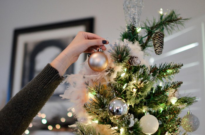 A woman's hand placing a bauble on a Christmas tree.
