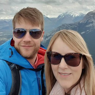 A young couple pose for a phone selfie on holiday, with snow-capped mountains in the background.