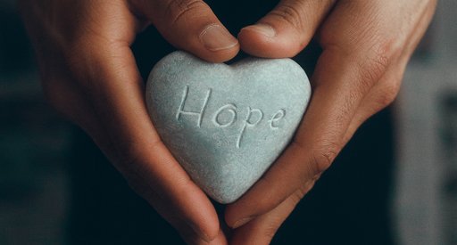 Image of hands holding a heart-shaped stone with the word "hope" carved on it.