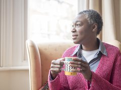 Older Black woman holding mug and looking into the distance