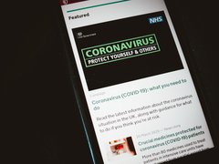 Close-up of a phone screen displaying an official Covid-19 article explaining 'what you need to do' from the NHS and HM Government.
