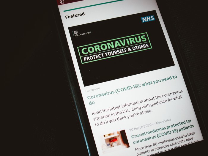 Close-up of a phone screen displaying an official Covid-19 article explaining 'what you need to do' from the NHS and HM Government.