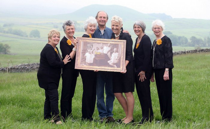 The Calendar Girls in a Yorkshire field posing with a man in front of one of their photos.