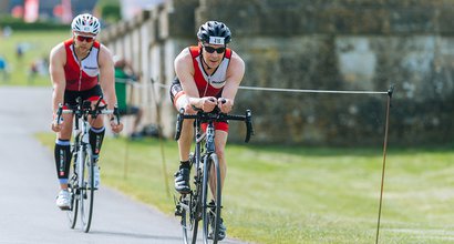 Two triathlon participants going downhill on bikes wearing Blood Cancer UK cycling tops.