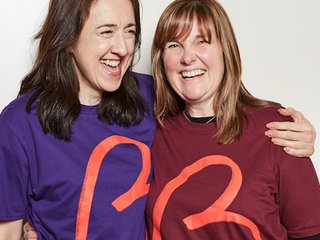 Two people laughing with their arms around one another wearing Blood Cancer UK branded t-shirts.
